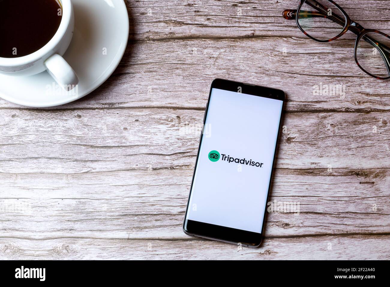 Ein Handy oder Handy auf einem Holz gelegt Tabelle mit der Tripadvisor Reisebericht App geöffnet neben Ein Kaffee Stockfoto