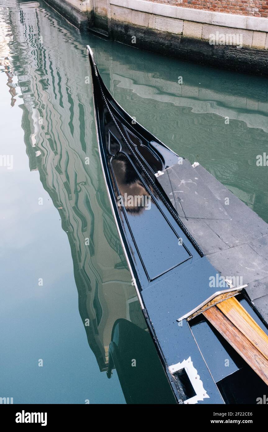 Vorderseite einer schwarz glänzenden Gondel auf einem Kanal in Venedig, Italien, zeigt die Spiegelung von Gebäuden in der Wasseroberfläche Stockfoto