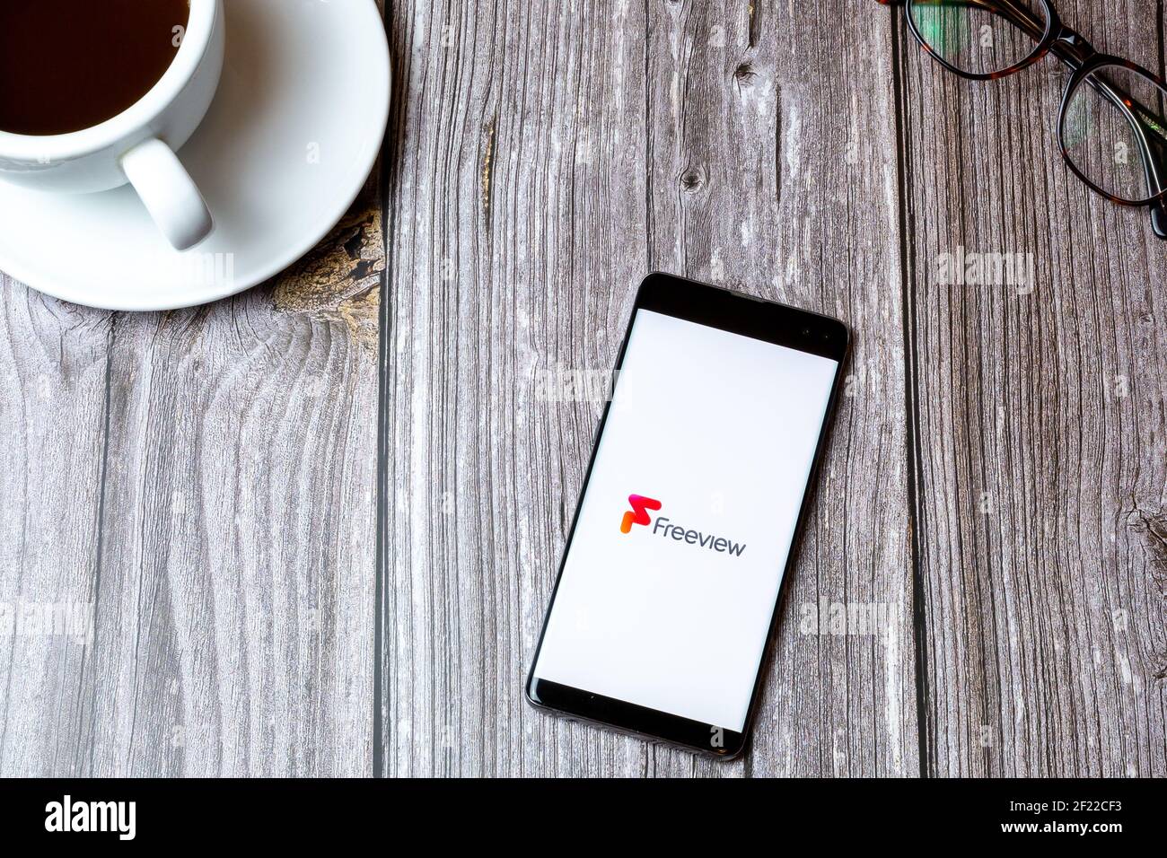 Ein Handy oder Handy auf einem Holz gelegt Tabelle mit der Freeview TV App auf dem Bildschirm als nächstes geöffnet Zu einem Kaffee Stockfoto