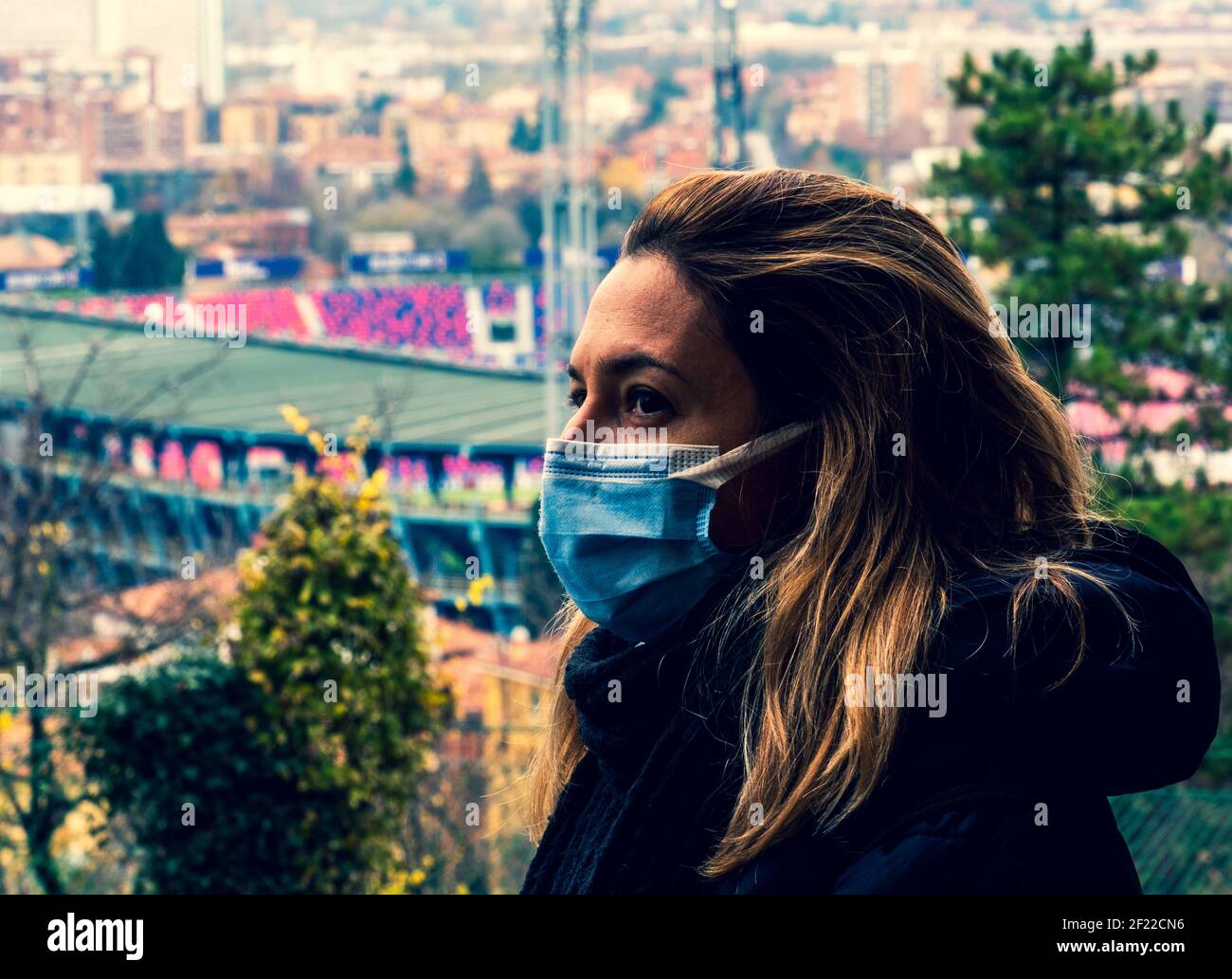 Frau mit Maske auf Gesicht Profilansicht besorgt über Coronavirus Pandemie mit Blick auf eine Stadt und Stadion in der Hintergrund Stockfoto