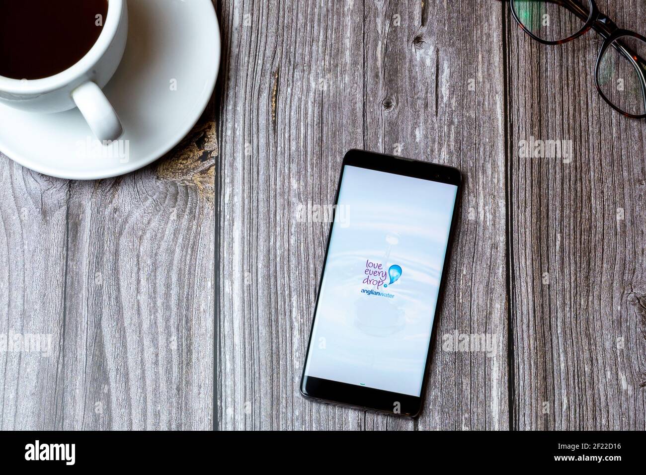 Ein Handy oder Handy auf einem Holz gelegt Tabelle mit der Anglian Wasser-App auf dem Bildschirm als nächstes geöffnet Zu einem Kaffee Stockfoto