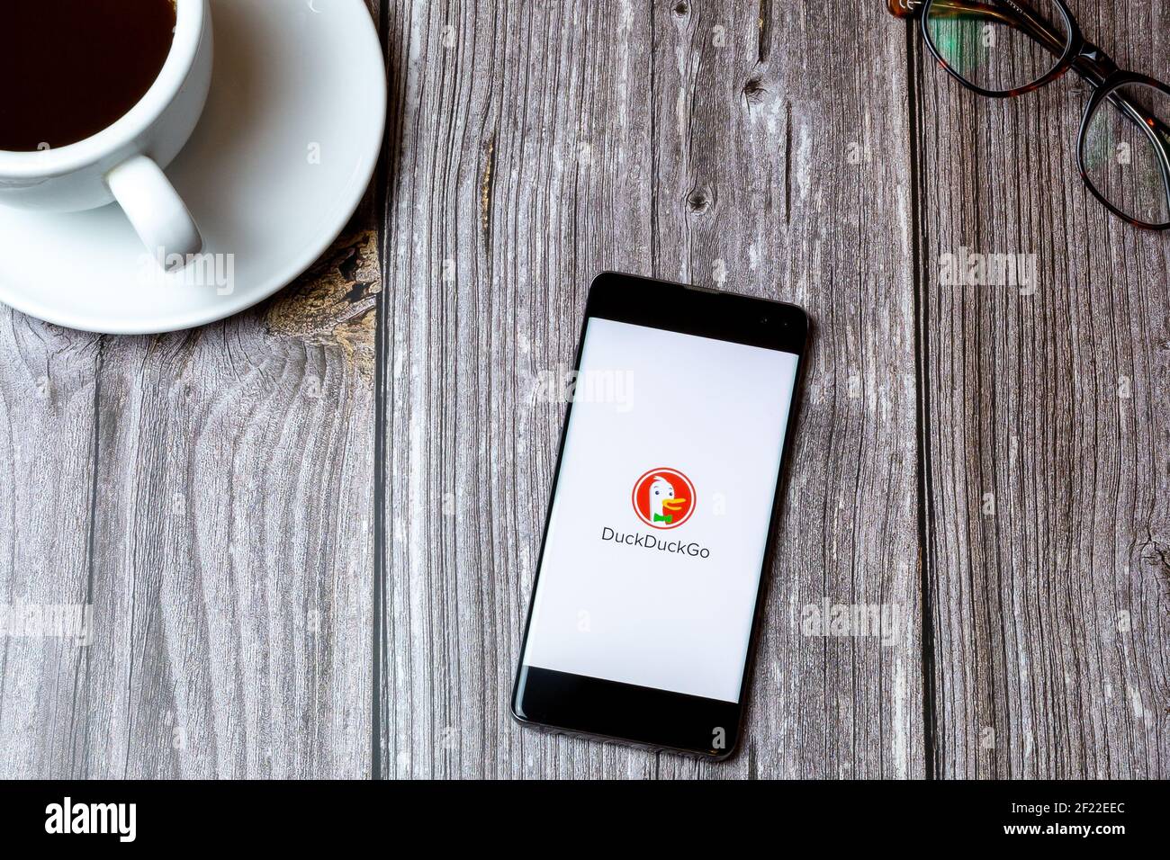 Ein Handy oder Handy auf einem Holz gelegt Tabelle mit der DuckDuckGo App auf dem Bildschirm neben geöffnet Ein Kaffee Stockfoto