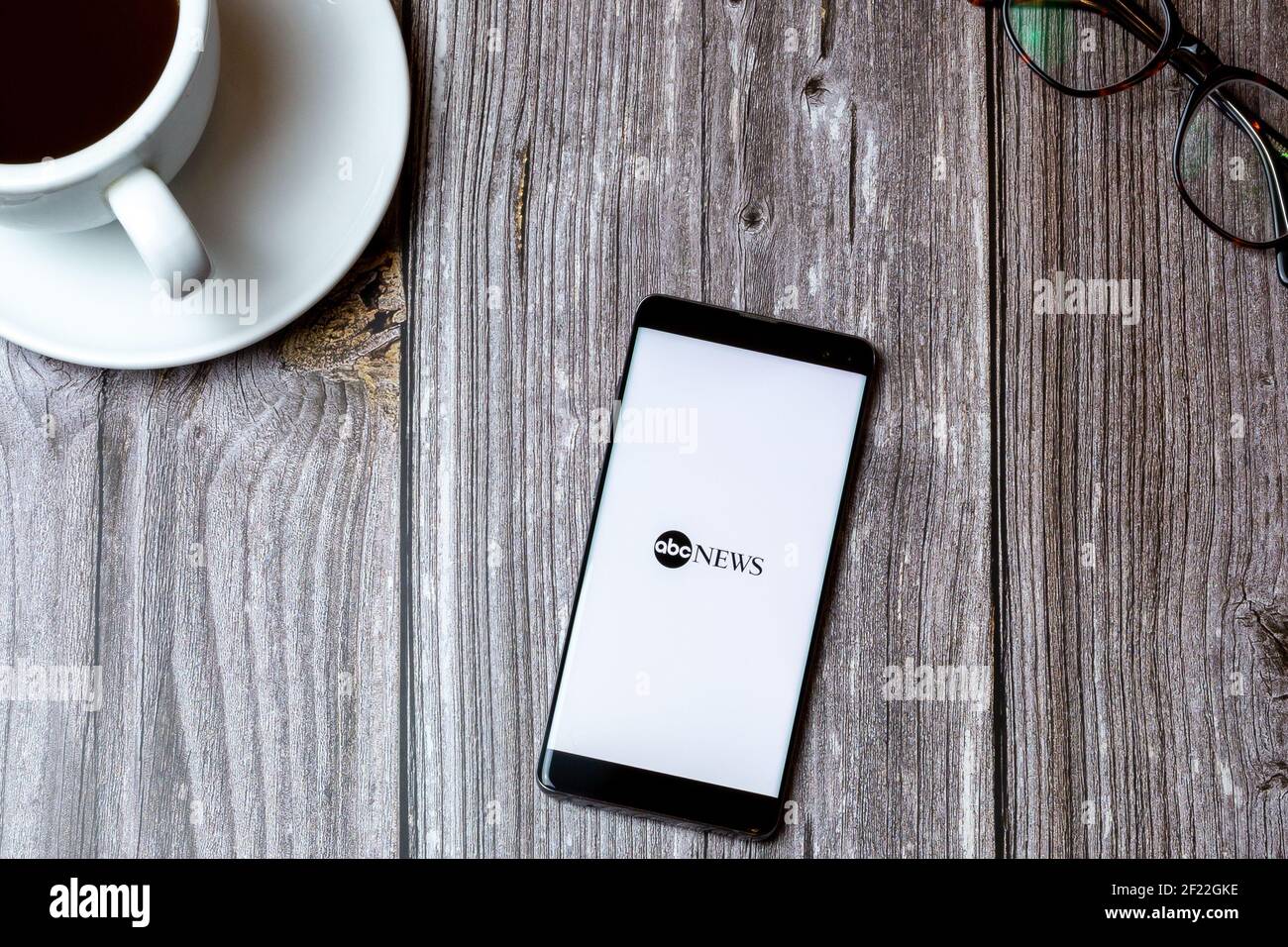 Ein Handy oder Handy auf einem Holz gelegt Tabelle mit der ABC News App auf dem Bildschirm als nächstes geöffnet Zu einem Kaffee Stockfoto