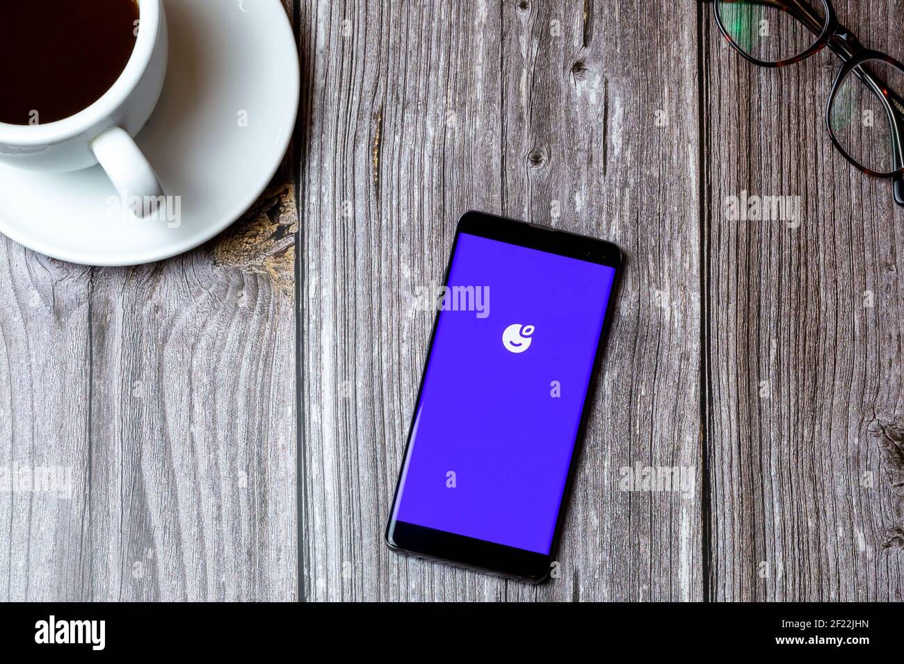 Ein Handy oder Handy auf einem Holz gelegt Tabelle mit der Plum saving App auf dem Bildschirm als nächstes geöffnet Zu einem Kaffee Stockfoto