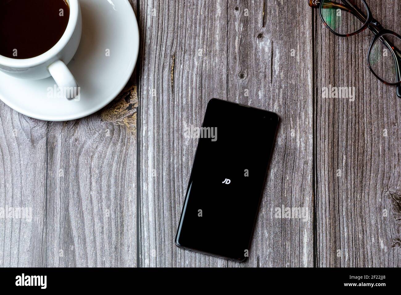 Ein Handy oder Handy auf einem Holz gelegt Tabelle, in der die JD-App auf dem Bildschirm neben geöffnet ist Ein Kaffee Stockfoto