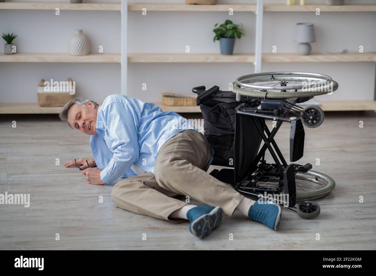 Behinderter älterer Mann, der auf dem Boden lag, nachdem sein Rollstuhl gestürzte Drinnen Stockfoto
