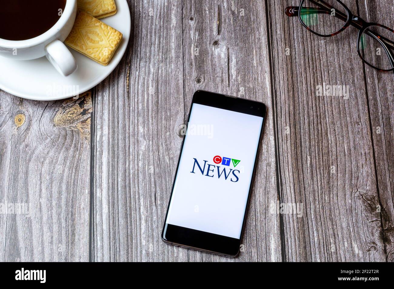 Ein Handy oder Handy auf einem Holztisch Mit der CTV News App neben einem Kaffee öffnen Und Brille Stockfoto