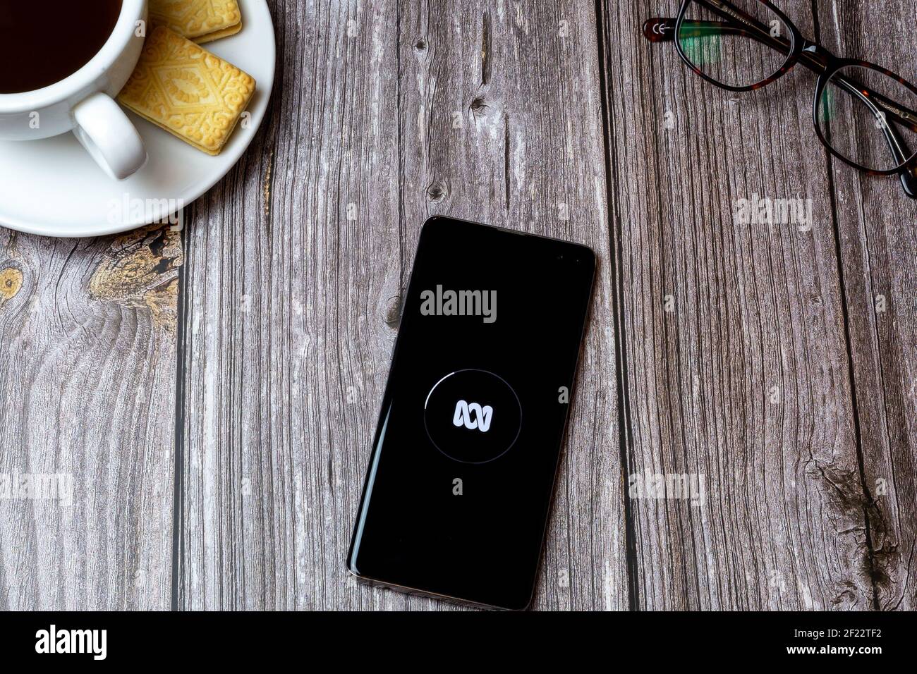 Ein Handy oder Handy auf einem Holztisch Mit der ABC News App neben einem Kaffee öffnen Und Brille Stockfoto