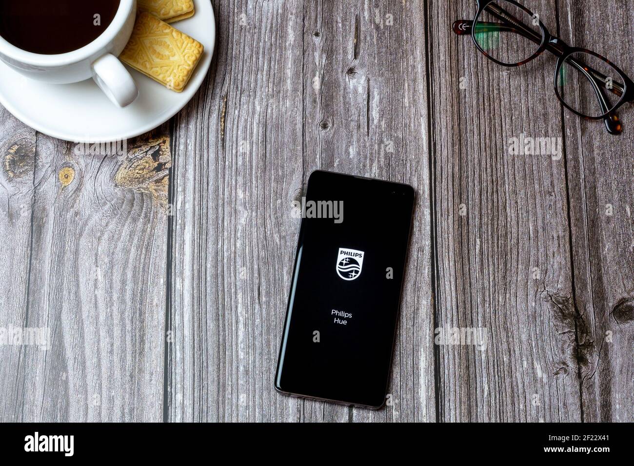 02-24-2021 Portsmouth, Hampshire, UK EIN Mobiltelefon oder Handy auf einem Holztisch mit der Philips Hue App, die neben einem Kaffee und einer Brille geöffnet ist Stockfoto