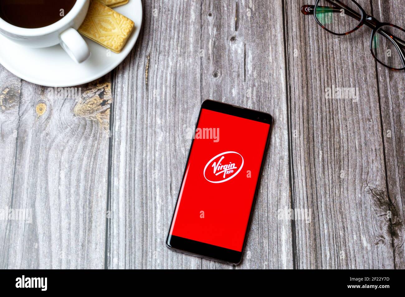 Ein Handy oder Handy auf einem Holztisch Mit der Virgin Red App neben einem Kaffee öffnen Und Brille Stockfoto