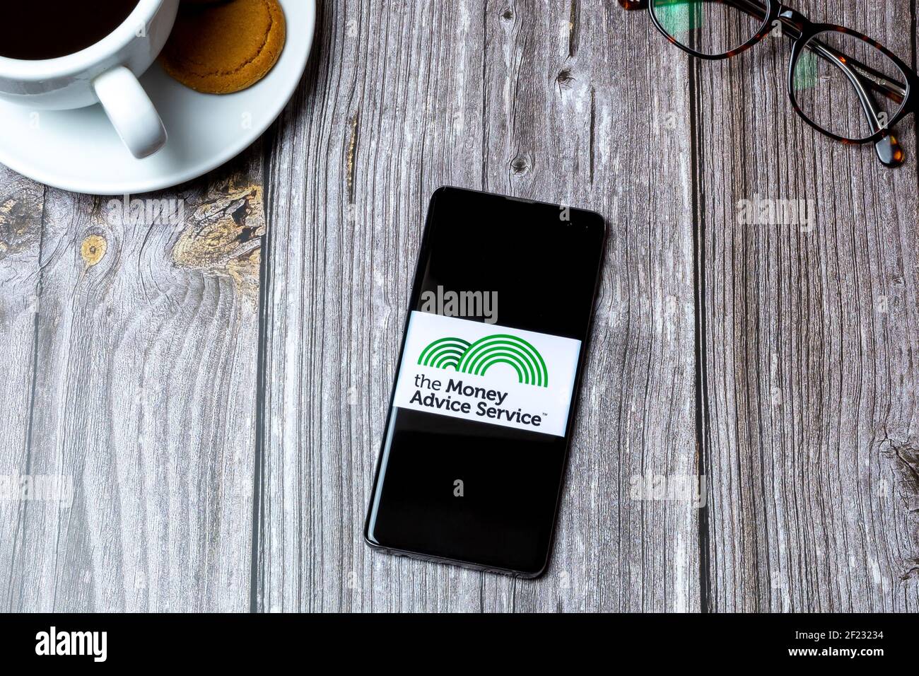 Ein Handy oder Handy auf einem Holz gelegt Tabelle mit dem Logo des Geldberatungsdienstes auf dem Bildschirm Stockfoto