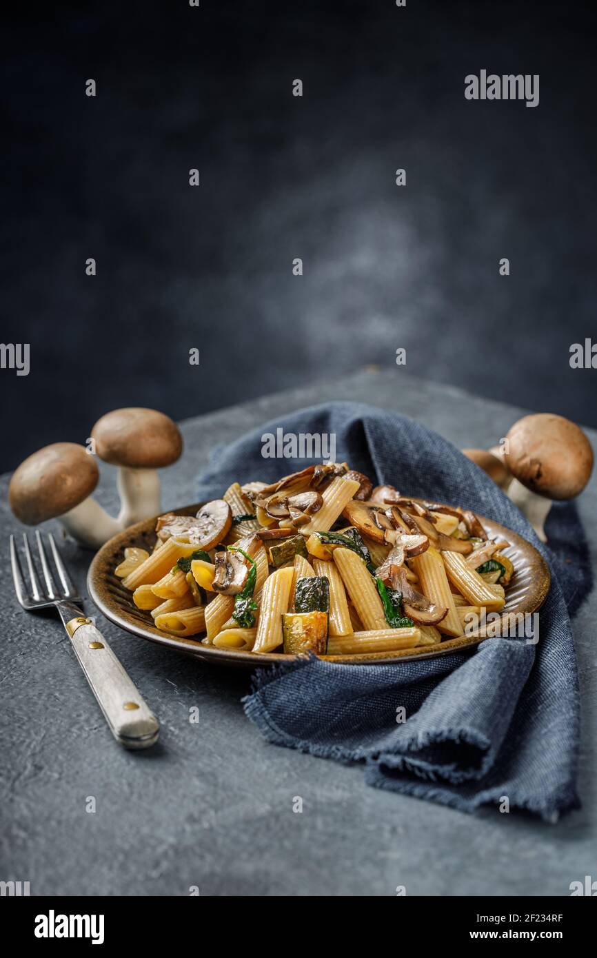 Pasta Penne mit gerösteten Pilzen, Knoblauch und Zucchini. Italienische Küche auf blauem Marmortisch. Stockfoto