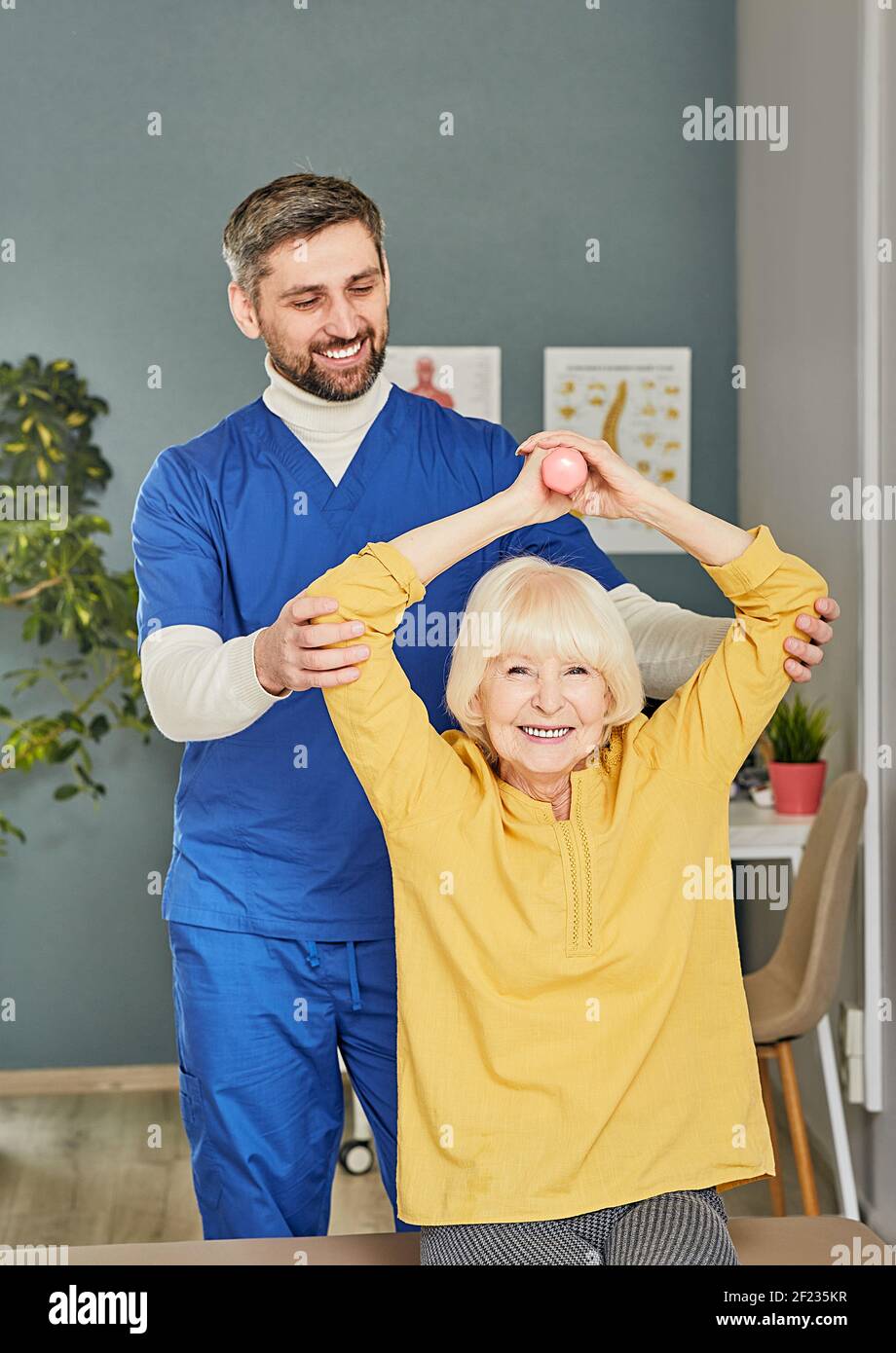 Der Arzt hilft, therapeutische Übungen für eine ältere Frau zu machen, um die Gesundheit der Oma zu verbessern. Ältere Frau mit Kurzhanteln in den Händen Stockfoto