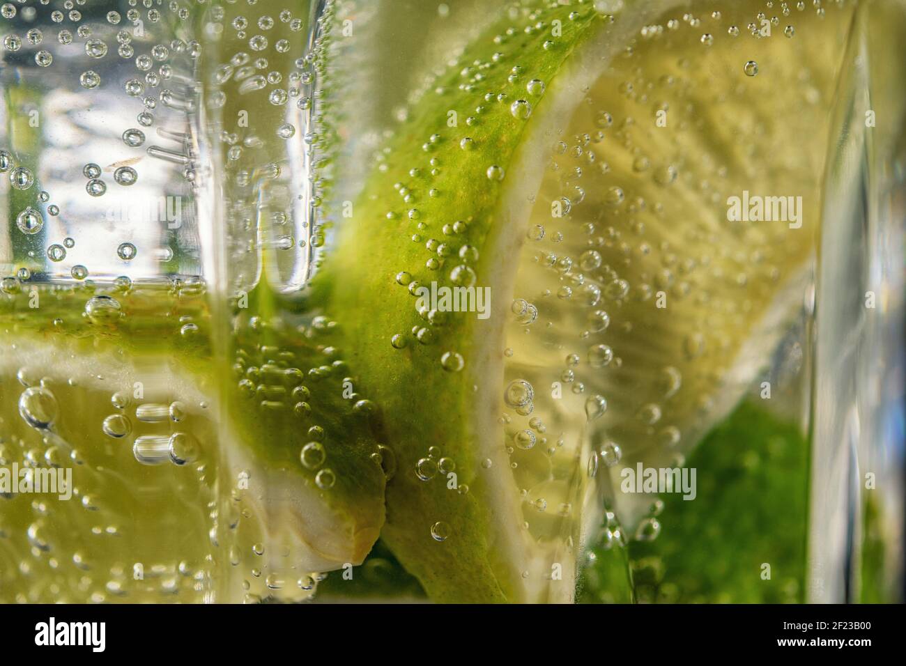 Limettenscheibe mit Tropfen in kohlensäurehaltiges Mineralwasser. Sommerdrink-Konzept. Stockfoto