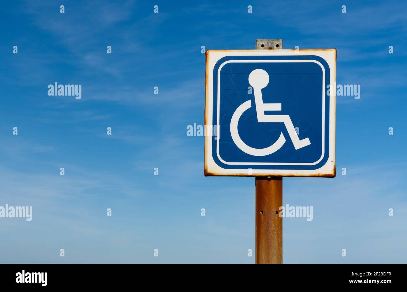 Nahaufnahme eines Behindertenparkplatzes schild mit verrosteten Kanten und blauem Himmel behin Stockfoto