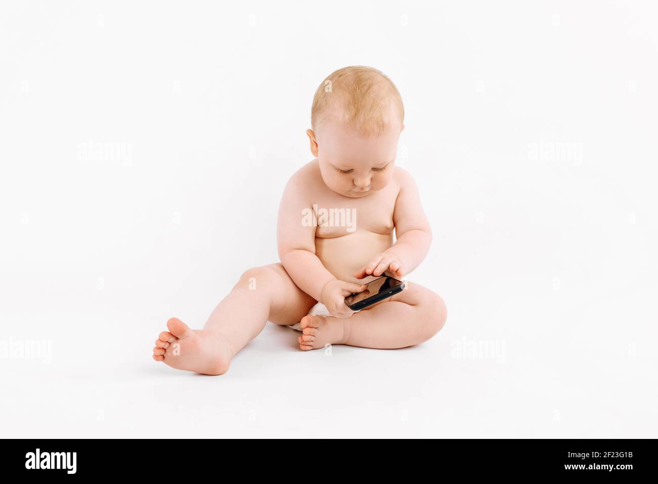 Kleines Baby in einer Windel, mit einem Handy sitzt auf einem isolierten weißen Hintergrund Stockfoto