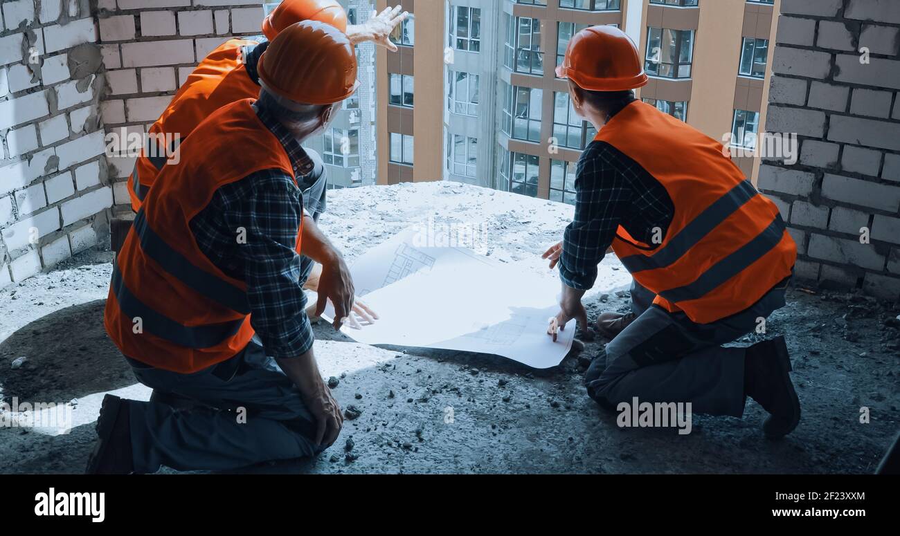 Bauherren in Hand Hüte diskutieren Blaupause, während auf der Konstruktion sitzen Standort Stockfoto