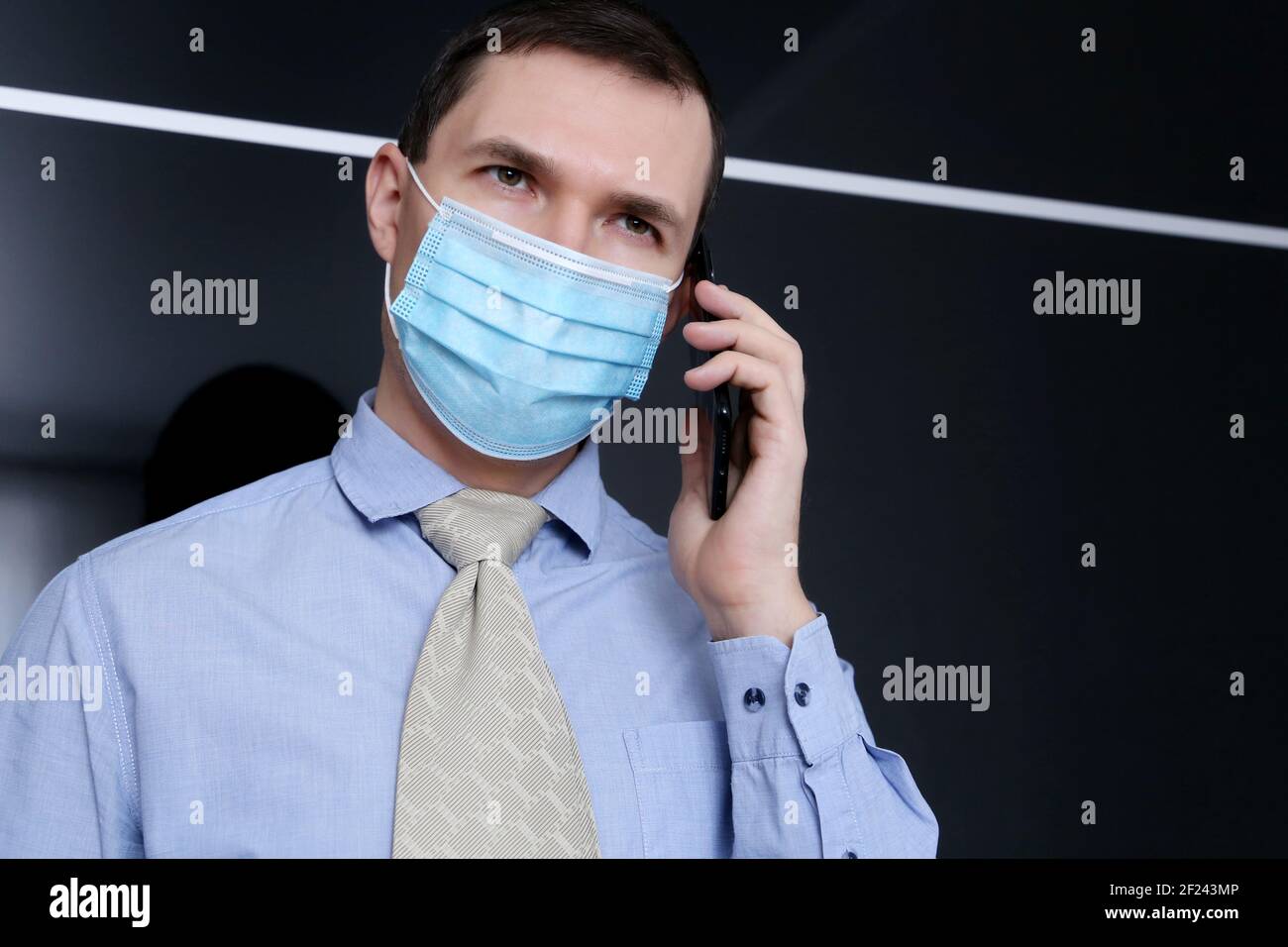 Porträt des Mannes in schützende Gesichtsmaske und Bürokleidung im Gespräch auf dem Handy, Smartphone in der männlichen Hand. Kommunikation während einer Coronavirus-Pandemie Stockfoto