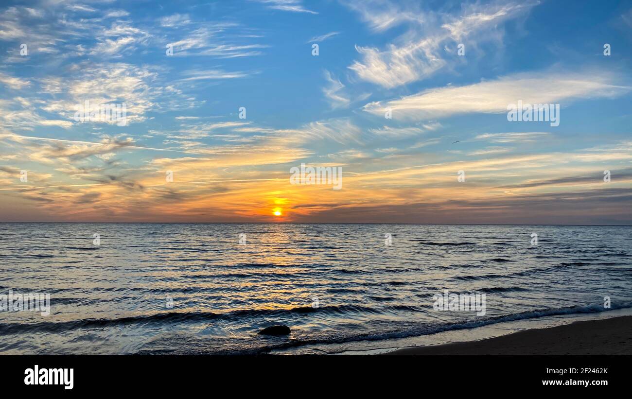 Sommeruntergang am Meer mit einem golden orangefarbenen Himmel und der Sonne durch die Wolken. Die Möwe Silhouette ist sichtbar. Der Strand Sand wird durch Meer w gewaschen Stockfoto