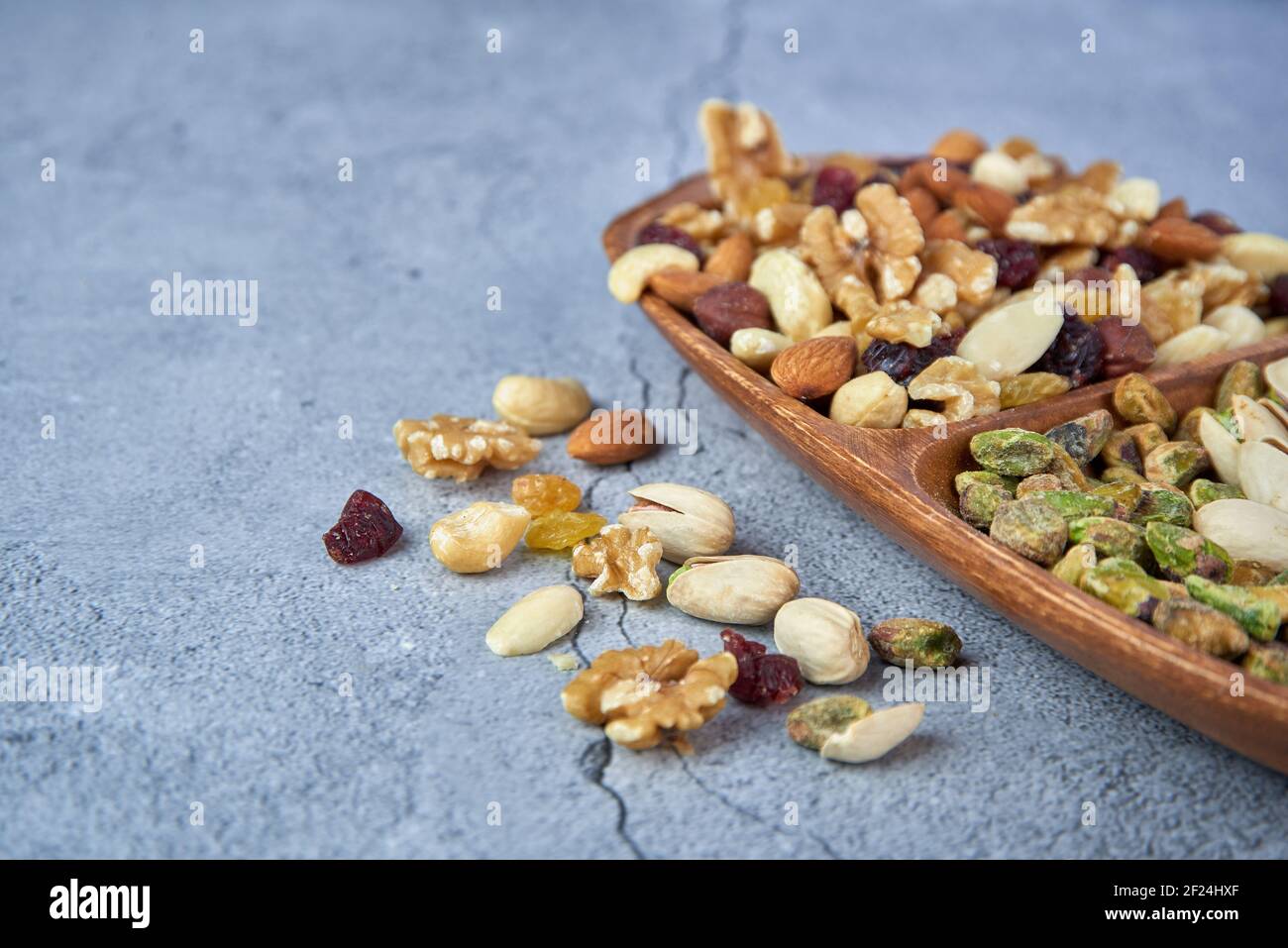 Getrocknete Früchte mit Nüssen, Pistazien, Cashewnüssen in Holzschüssel auf grauem Betongrund mischen. Stockfoto