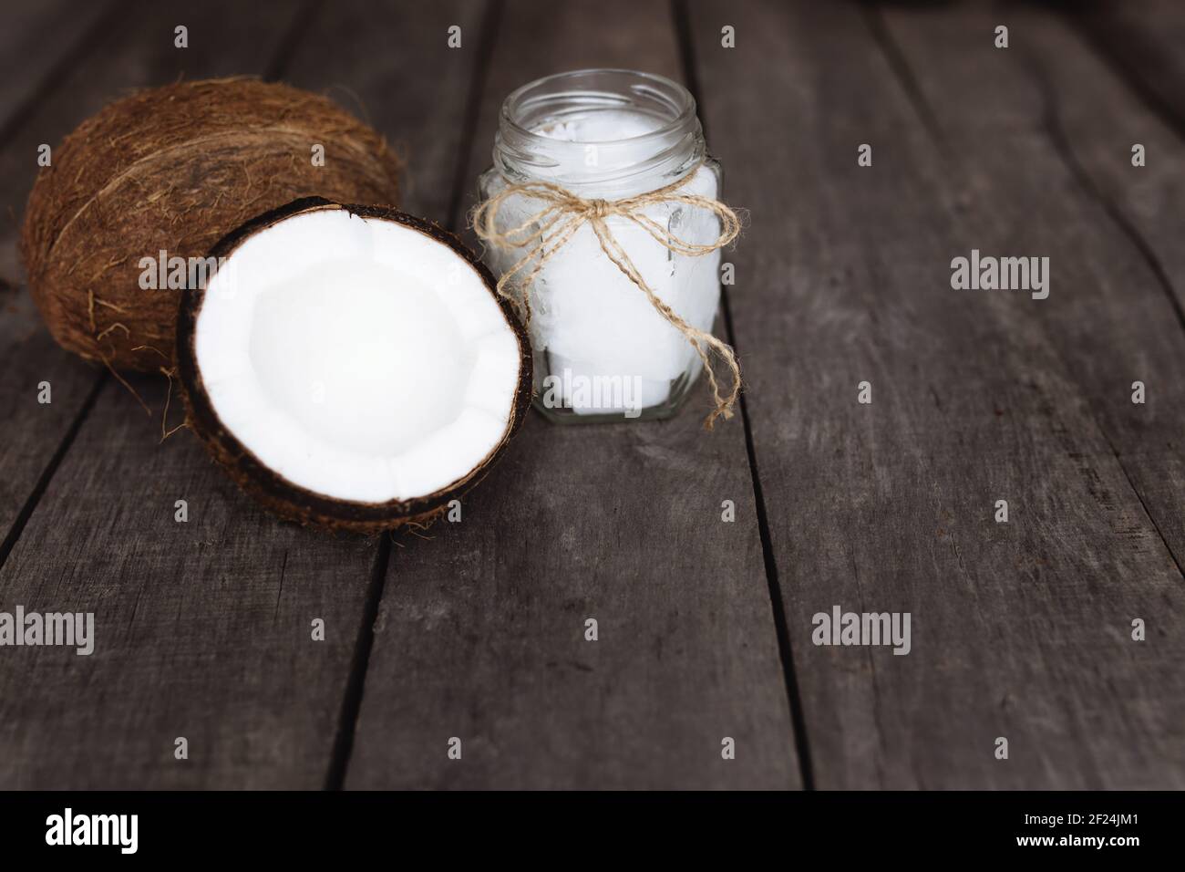 Zerbrochene Kokosnüsse auf grauem Holzhintergrund mit Glas rohem Bio-Kokosöl extra vergine. Weißes Kokosnusspulpe. Hochwertige Fotos Stockfoto
