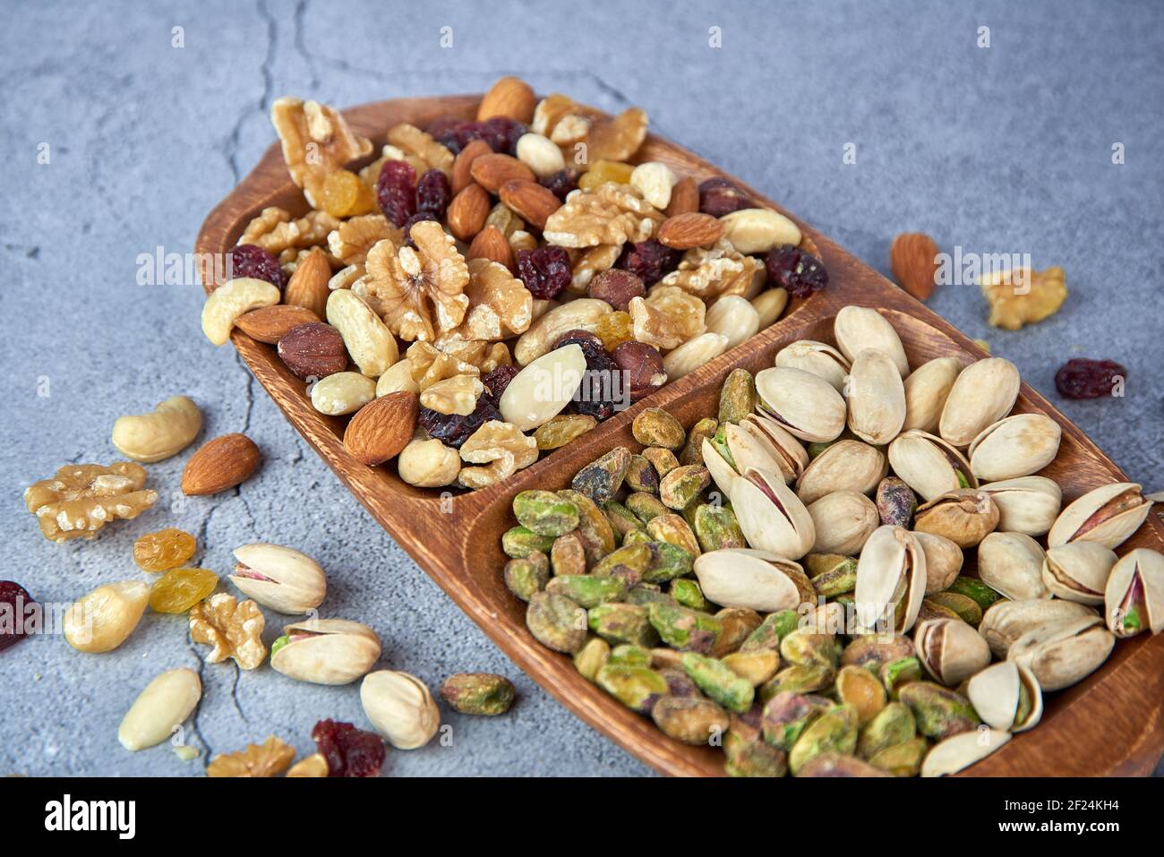 Getrocknete Früchte mit Nüssen, Pistazien, Cashewnüssen in Holzschüssel auf grauem Betongrund mischen. Stockfoto