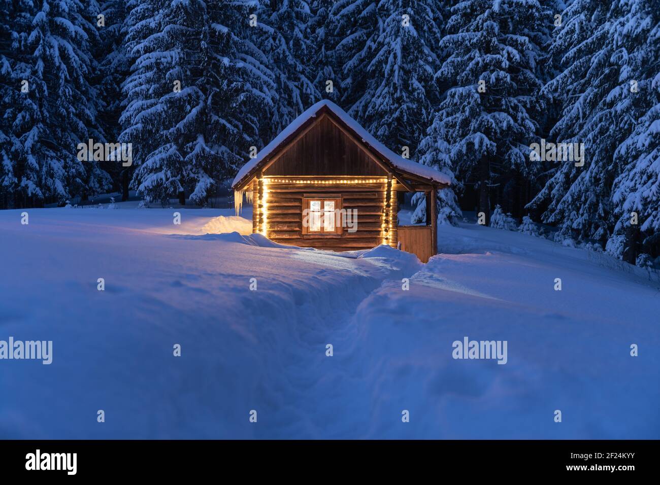 Fantastische Winterlandschaft mit glühender Holzhütte im verschneiten Wald. Gemütliches Haus in den Karpaten. Weihnachtsfeiertagskonzept Stockfoto