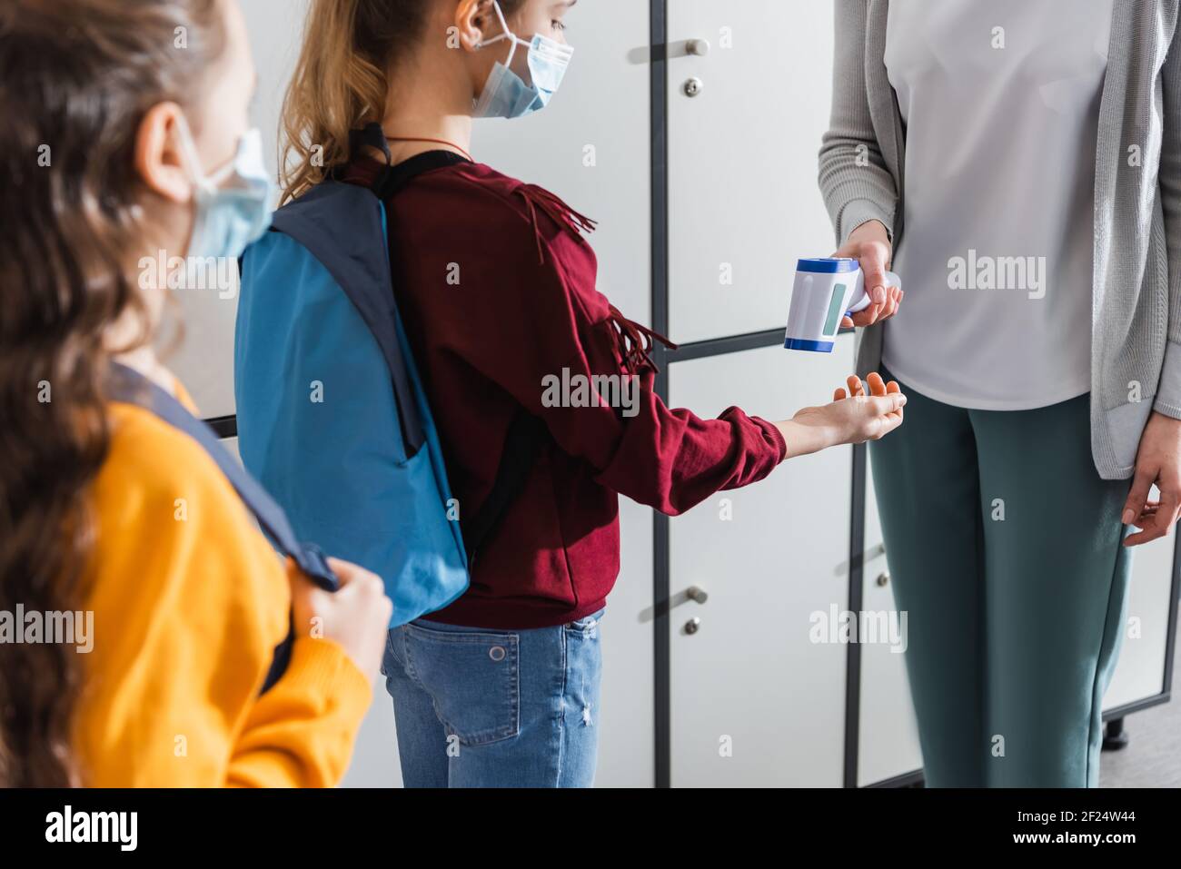 Lehrer mit Infrarot-Thermometer auf Schüler in medizinische Maske mit Rucksack Stockfoto