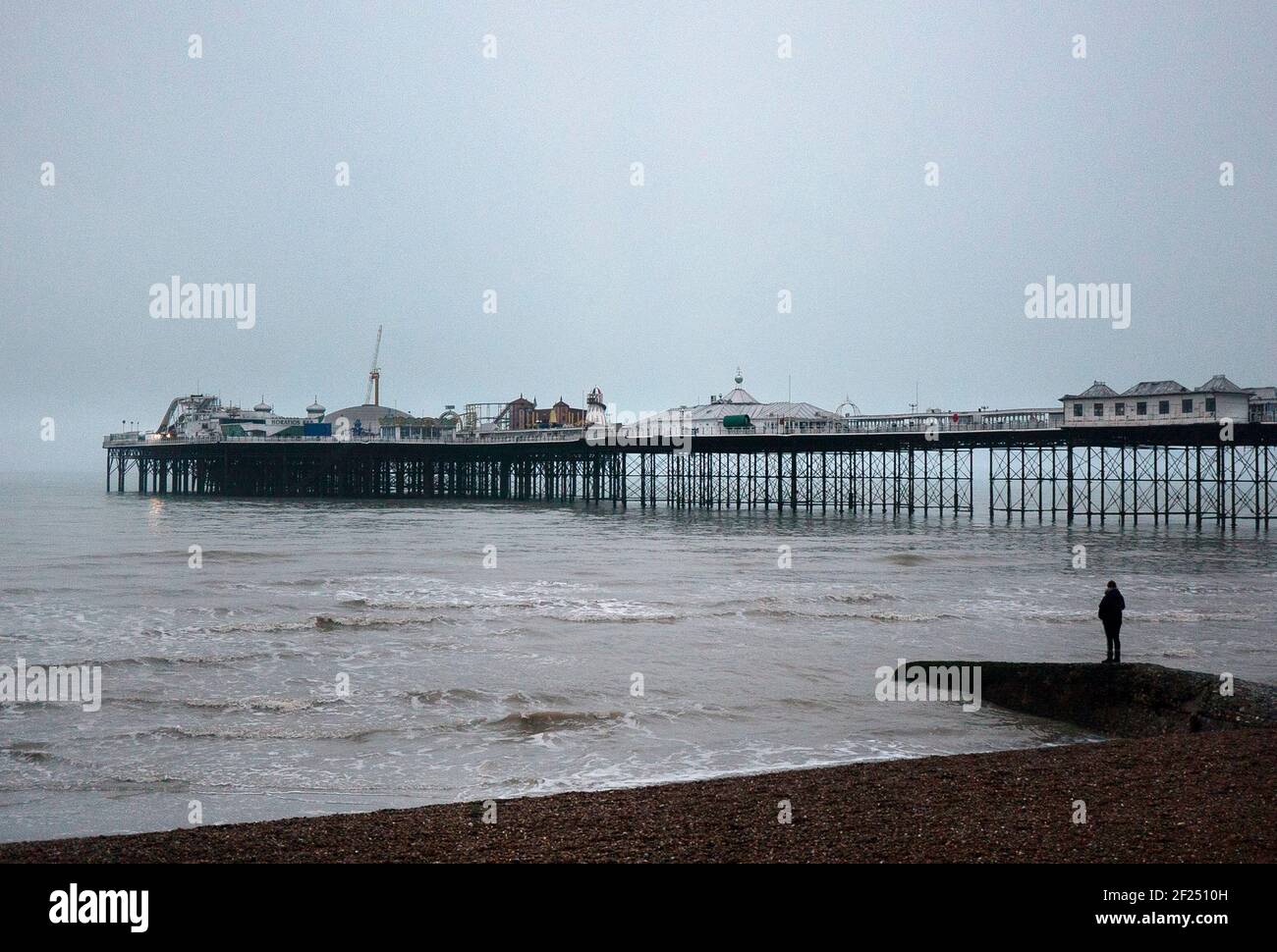 Der Palace Pier Brighton an EINEM kalten Winters Abend mit Eine einzelne Person, die mit dem Rücken zur Kamera steht Auf EINEM Groyne im Vordergrund Stockfoto