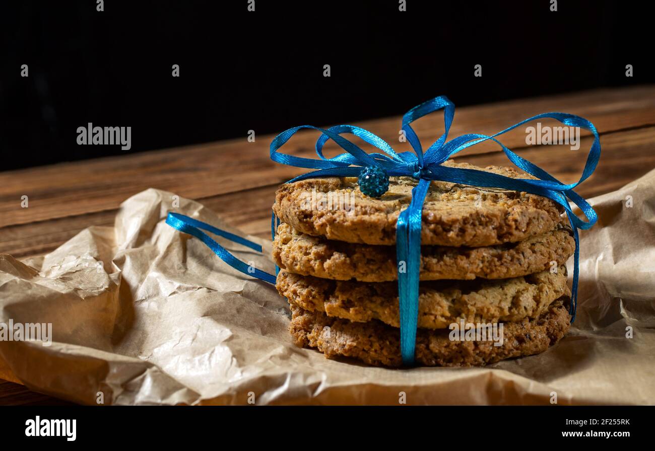 Hausgemachte Haferflocken Cookies auf Pergamentpapier mit einem blauen Band gebunden, Geschenkverpackung, Dekoration. Holzhintergrund. Platz für Text, Seitenansicht. Stockfoto