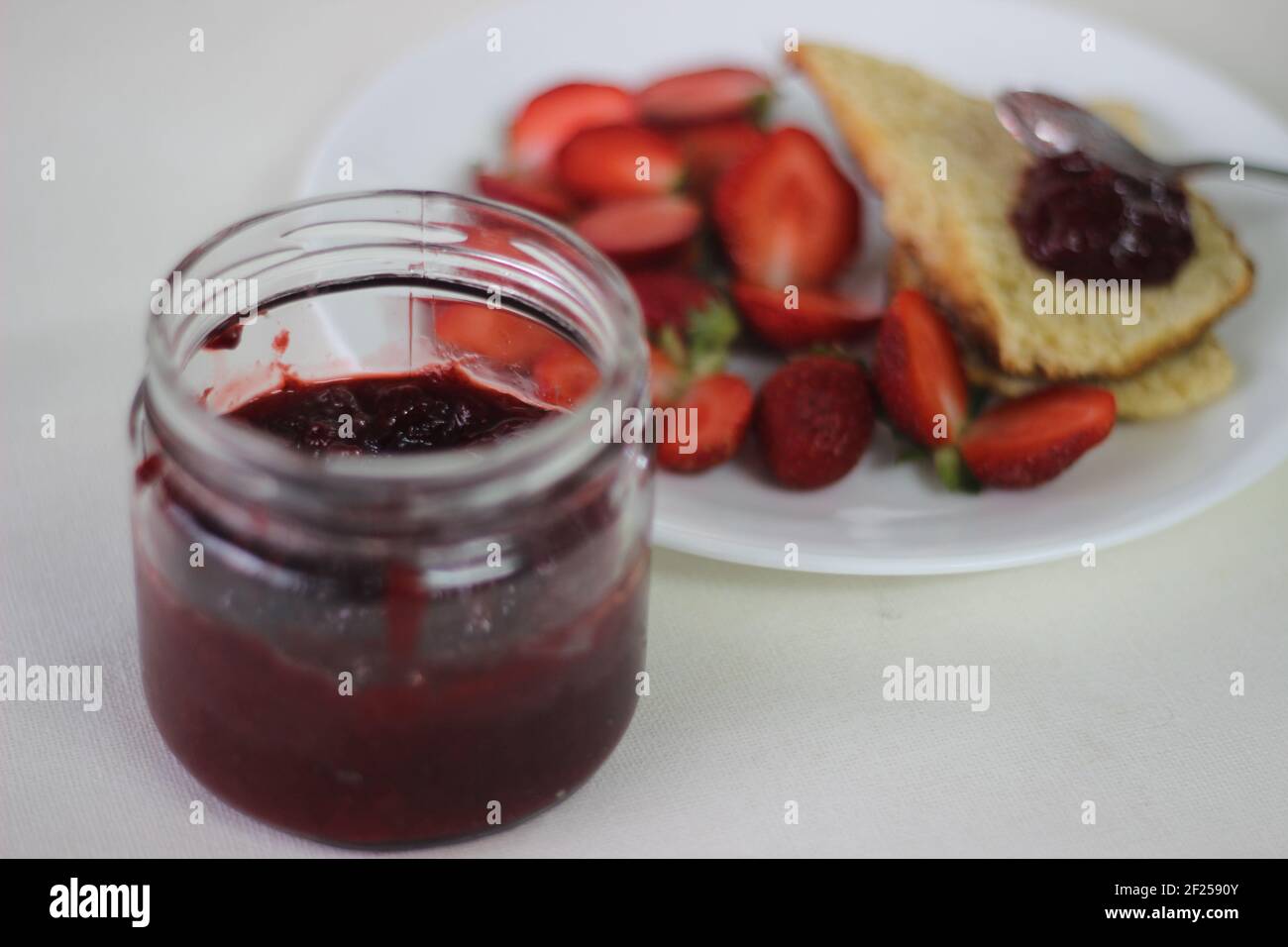 Halb-volle Flasche mit hausgemachter Erdbeermarmelade Schuss zusammen mit hausgemachten einfach milde Buttermilch Scones. Aufnahme auf weißem Hintergrund Stockfoto