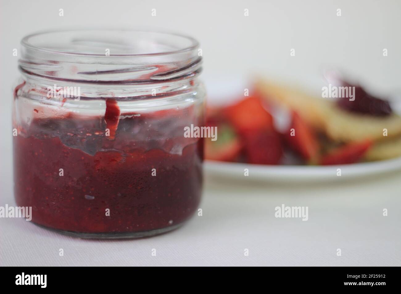 Halb-volle Flasche mit hausgemachter Erdbeermarmelade Schuss zusammen mit hausgemachten einfach milde Buttermilch Scones. Aufnahme auf weißem Hintergrund Stockfoto