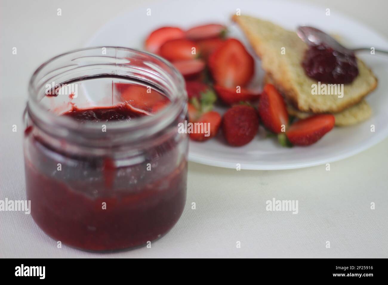 Halb-volle Flasche mit hausgemachter Erdbeermarmelade Schuss zusammen mit hausgemachten einfach milde Buttermilch Scones. Aufnahme auf weißem Hintergrund Stockfoto