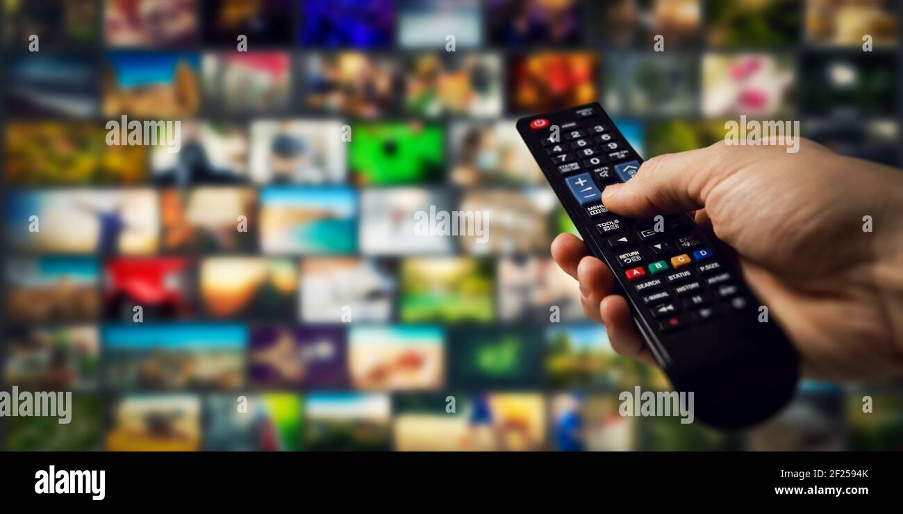 tv-Kanäle im Hintergrund und Fernbedienung in der Hand. Smart-TV und Content-on-Demand-Konzept Stockfoto