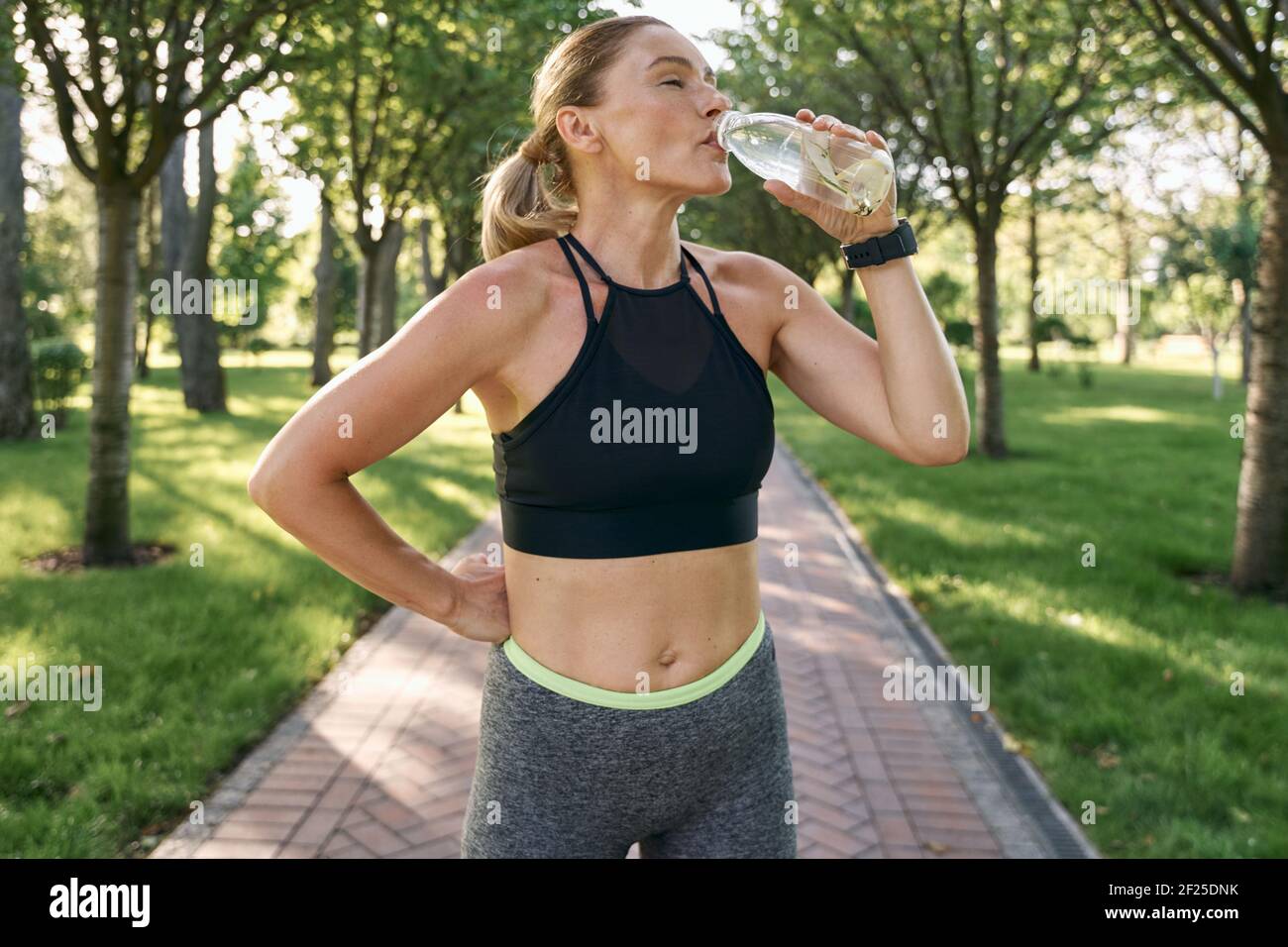 Hydratation. Durstige sportliche Frau in Sportbekleidung Trinkwasser nach dem Joggen in einem grünen Park an einem sonnigen Sommertag Stockfoto