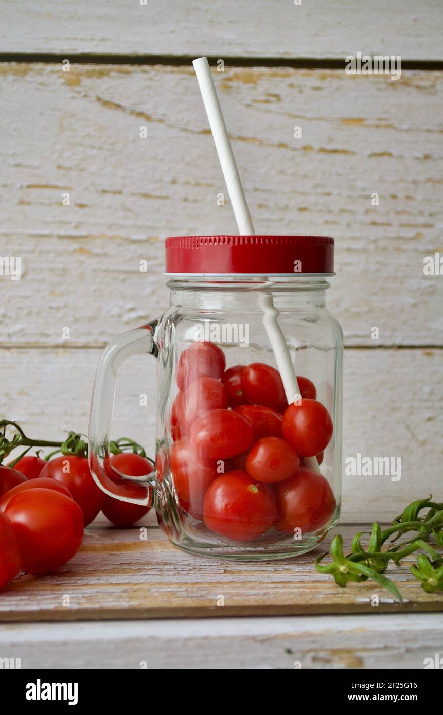 Nahaufnahme von Kirschtomaten in einem Schraubglas mit einem Roter Deckel vor einer weißen Holzwand Stockfoto