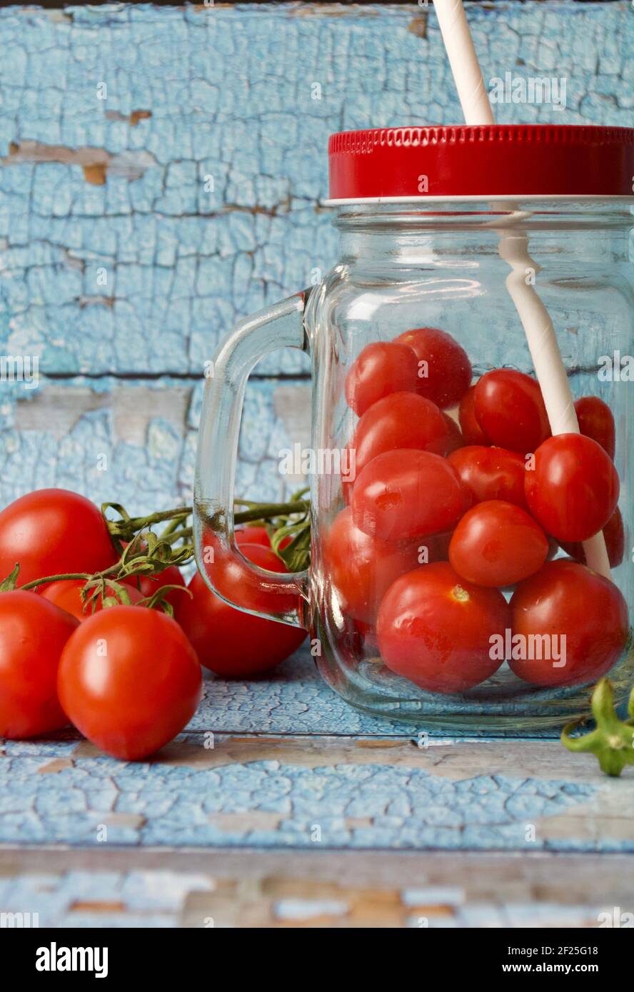 Frische kleine Tomaten neben einem gefüllten Glas mit Tomaten Vor einer blauen Holzwand Stockfoto