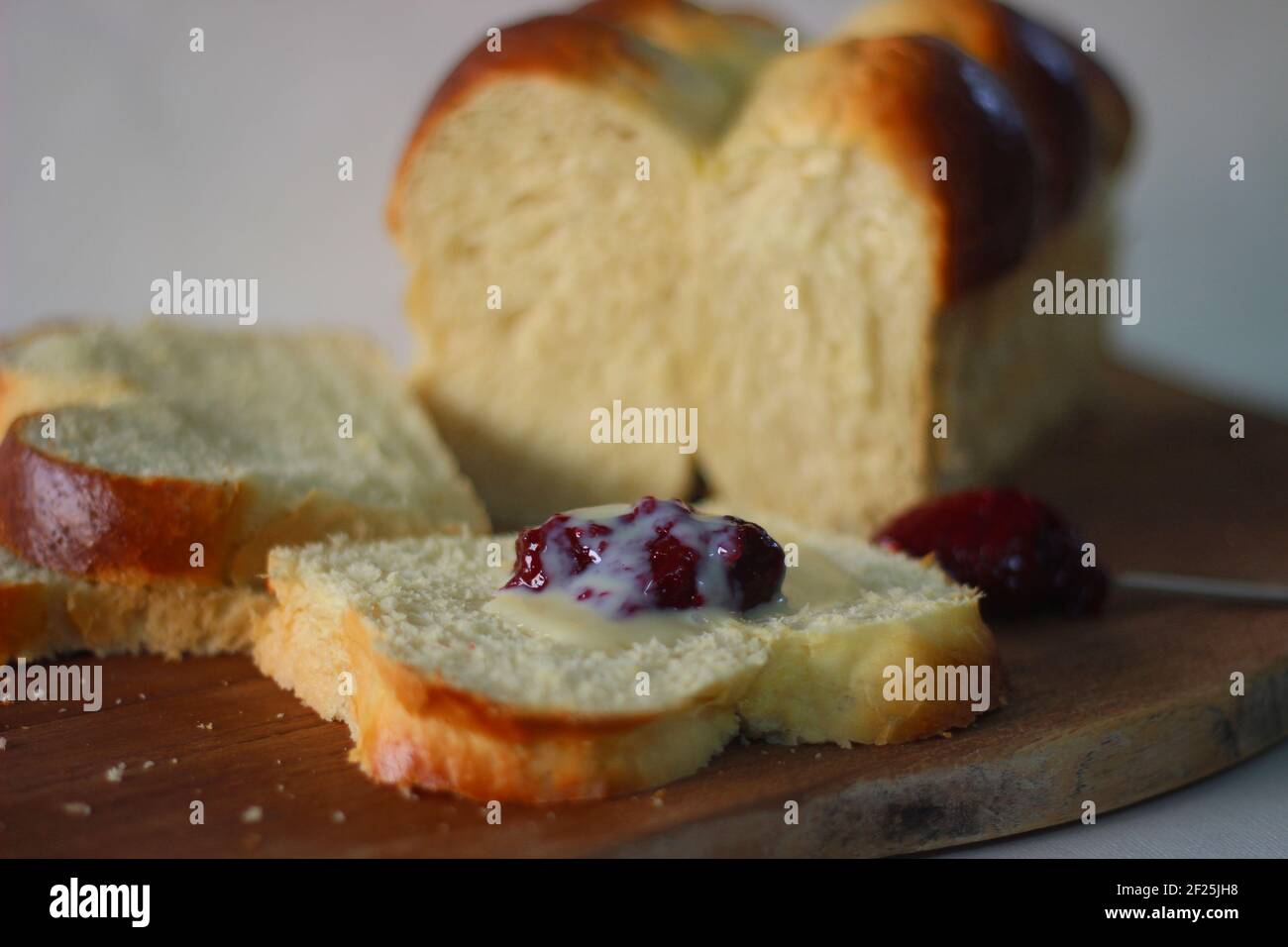 Frisch gebackener Brioche-Brötchen-Laib in Scheiben geschnitten und auf einem Holzbrett aufbewahrt. Serviert mit Marmelade. Aufnahme auf weißem Hintergrund. Stockfoto