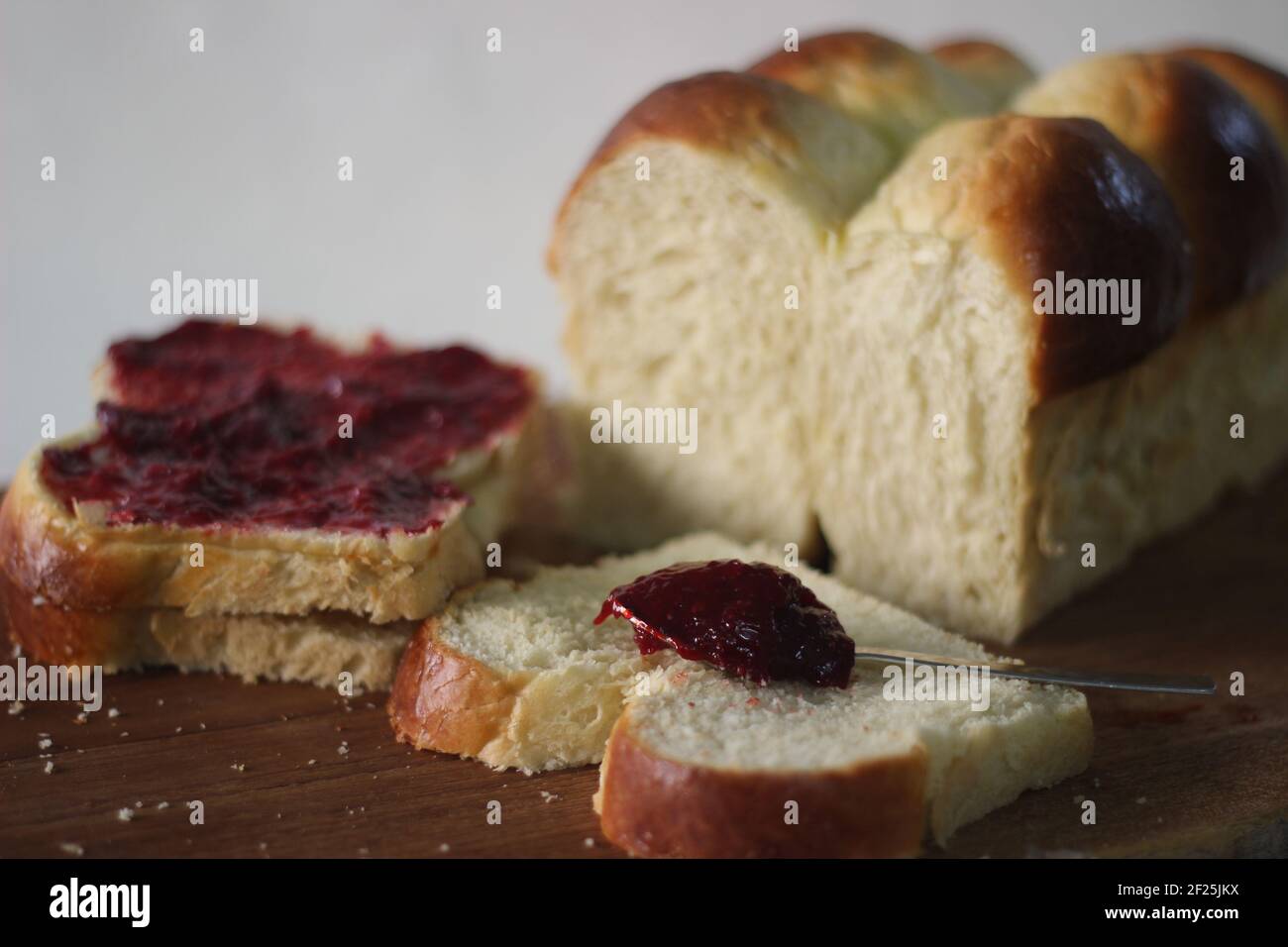 Frisch gebackener Brioche-Brötchen-Laib in Scheiben geschnitten und auf einem Holzbrett aufbewahrt. Serviert mit Marmelade. Aufnahme auf weißem Hintergrund. Stockfoto