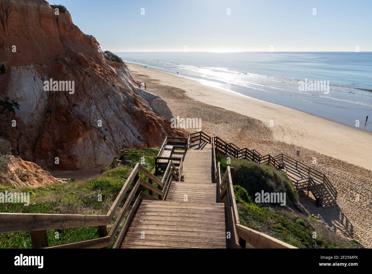 Eine lange Holzpromenade Zugang zum Strand führt hinunter zu einem Breiter goldener Strand mit bunten Sandklippen Stockfoto