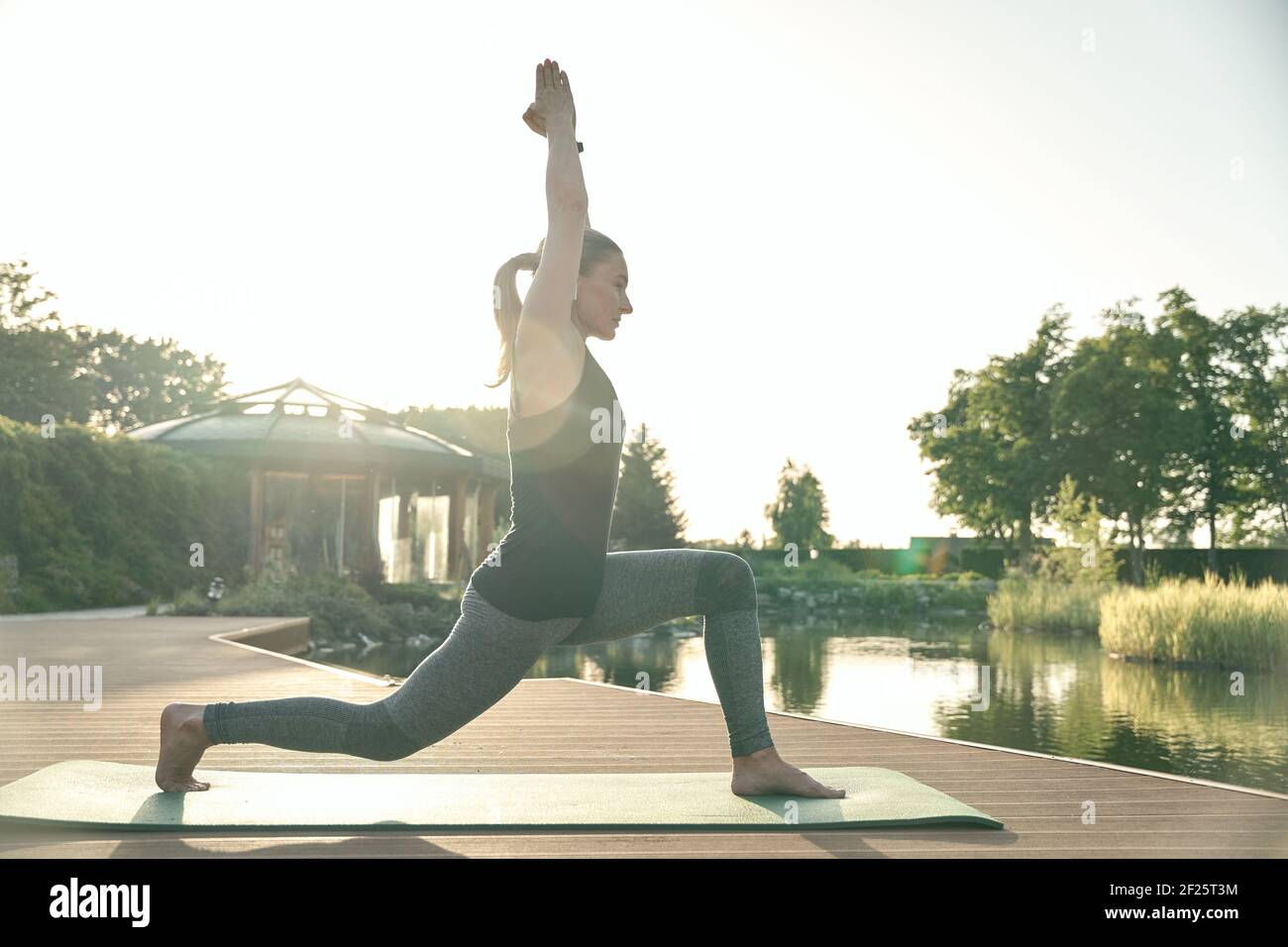 Verbessern Sie sich. In voller Länge Aufnahme einer entspannten Frau, die in Yoga-Pose steht, während sie Yoga auf einer Matte in der Natur macht Stockfoto