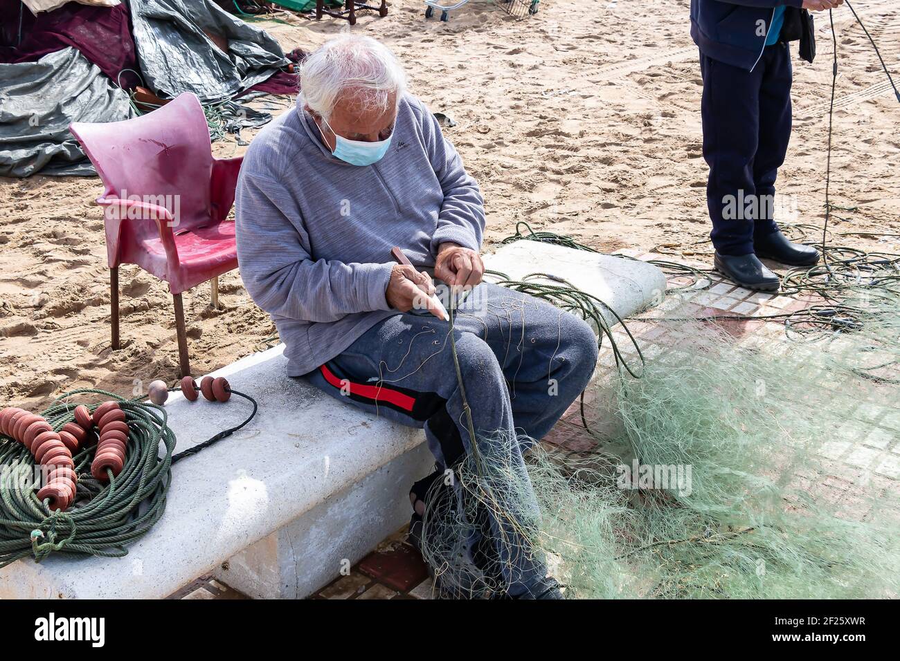 Huelva, Spanien - 27. Februar 2021: Ein Fischernetz wird von einem Fischer mit einem Messer repariert Stockfoto