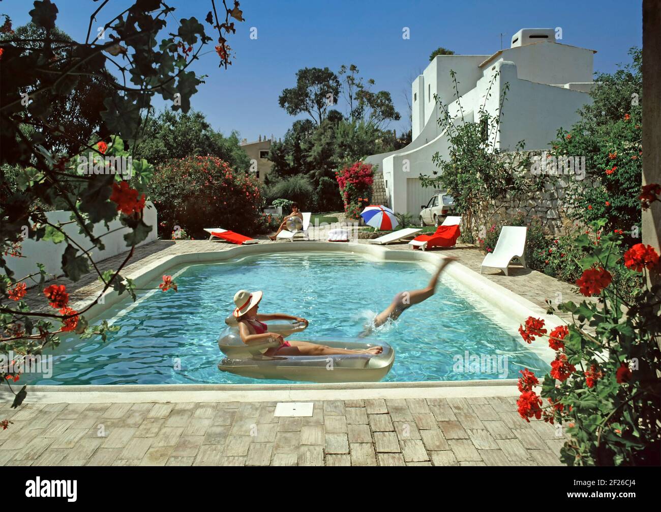 Historisches Archiv 1985 Ansicht aller Zutaten für ein erfolgreiches portugiesisches Modell veröffentlicht Familienpaket Sonnenschein Villa Urlaub in Die Algarve mit schönem private1980er-m-Swimmingpool und Gartenblumen in heißem blauen Himmel, sonniges Sommerwetter, Mietwagen Weißes, cooles, modernes Mietshausgebäude mit Mama, die sich auf den Sonnenliegen am Pool entspannen, Teenager, der taucht und nervt Meine Tochter sonnte sich auf einem schwimmenden Sessel, Lilo, und Dad machte 80s Archivfotos in einem „Way we were“-Bild, das es auch gab Fast alles für Auslandsreisen in Portugal Stockfoto