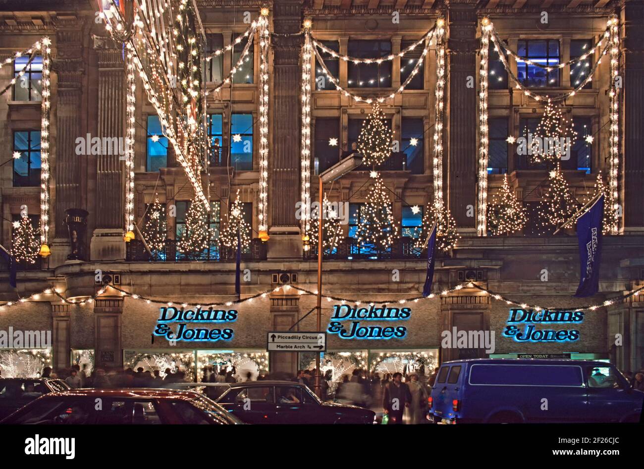 Historische 1985 Archiv Nachtansicht von Dickins & Jones hoch Qualitäts-Kaufhaus mit Gebäude Shop Front und dekoriert Weihnachten Bäume eingeschaltet Beleuchtung im berühmten Regent Street West End Einkaufsviertel unvermeidlich 1980s Stau & Bürgersteig Massen Käufer beleuchteten das Logo der Handelsmarke über jedem Fenster in Ein Archivbild aus dem Jahr 80s von der Art und Weise, wie wir uns befanden Weihnachten in London England Stockfoto