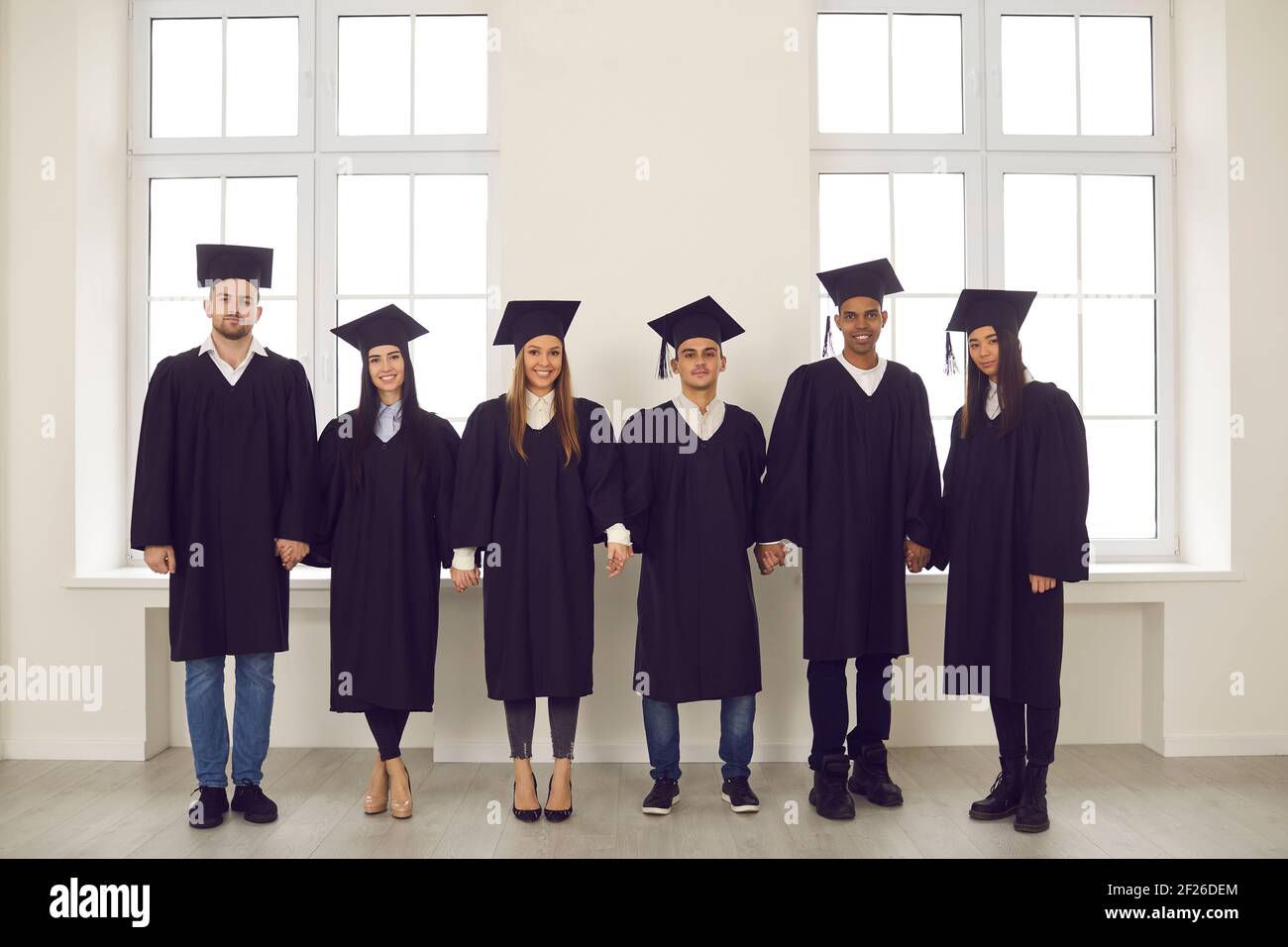 Porträt einer Gruppe von multirassischen Hochschulabsolventen in akademischen Kleidern, die Hände halten. Stockfoto