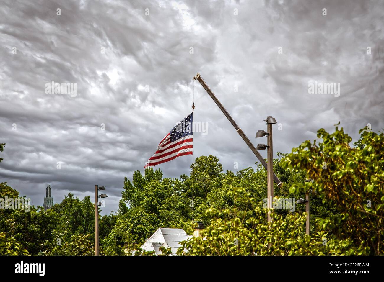 Baukran verwendet, um riesige amerikanische Flagge über Dächer fliegen Und Baumwipfel mit Downtown Wolkenkratzer in der Ferne - bewölkt dramatisch Himmel und selektiver Fokus Stockfoto