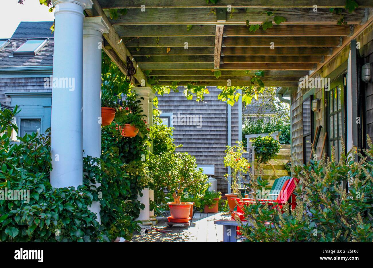 Klappbretthaus mit schattiger Veranda mit Pergola Dach mit Trauben Reben und andere Pflanzen wachsen in Fülle und bunten Adirondack Stühle Stockfoto