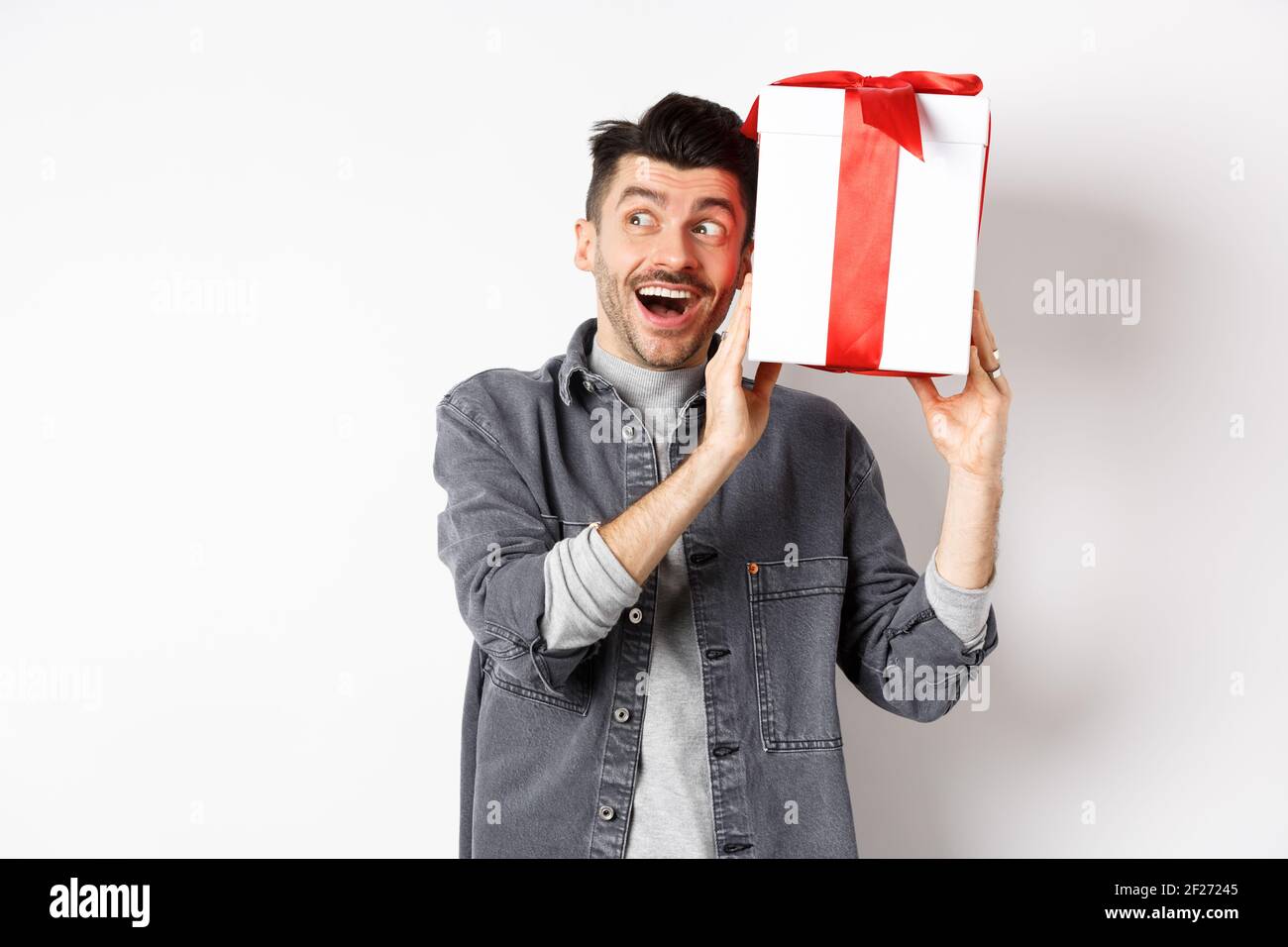 Glücklicher Freund schüttelt sein Geschenk, um zu erraten, was in, erhalten  Überraschung Geschenk am Valentinstag, lächelnd und Blick zur Seite che  Stockfotografie - Alamy