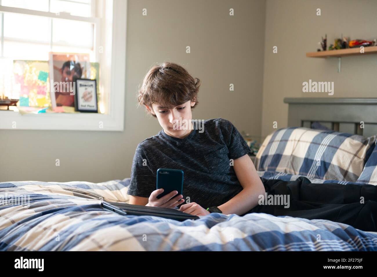 Tween Junge auf dem Bett mit Telefon und Tablet. Stockfoto