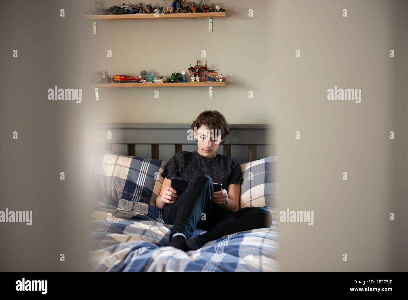 Blick durch die Tür zu Tween Junge auf seinem Bett mit einem Tablet sitzen. Stockfoto